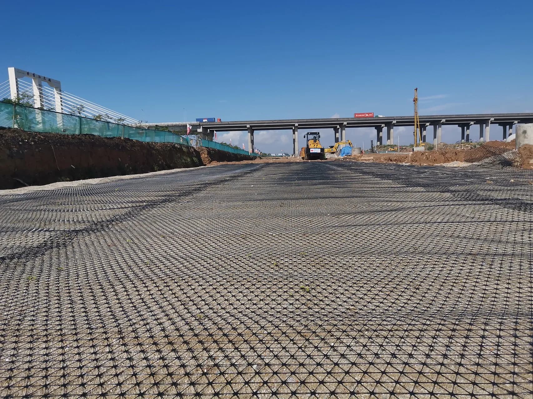 Triaxial geogrid laid across a granular working platform, with compaction plant working at the far end.